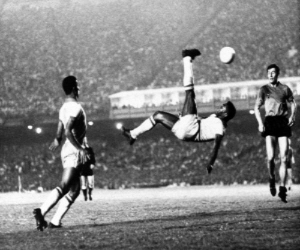 Black and white photo of a soccer player performing a bicycle kick during a match.